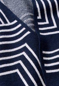 Stickad tyg med marinblå och vita geometriska ränder. Mjuk textur med kontrasterande ljusgrå mönstrade sektioner.