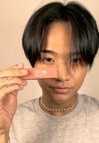 Ferskenfarget leppestift emballasje med matt finish, som viser etiketten "240 THE LIPSTICK" i hvitt, holdt av en person.