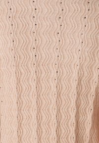 Tissu tricoté rose clair avec un motif en zigzag et de petits trous, créant une surface texturée et respirante.