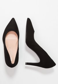 Zapatos de tacón alto negros con diseño de punta afilada, confeccionados en un material similar al ante, que presentan una silueta elegante y un acento en el tacón brillante.