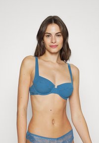 Sutiã azul acolchoado com riscas verticais e detalhes em renda. Apresenta alças ajustáveis e um fecho com gancho na frente. Adequado para uso diário.
