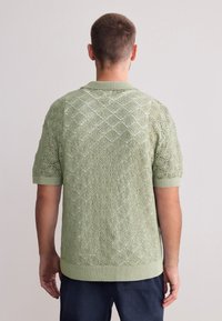 Stickad kortärmad tröja i ljusgrönt, med diamantmönster och texturerat tyg samt ribbad fåll och krage.