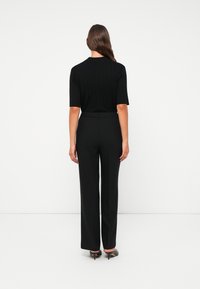 Svart ribbet topp med kort erm kombinert med svarte vide bukser. Antrekket har et elegant design og en glattere tekstur.