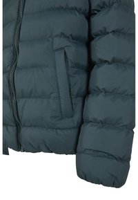 Doudoune bleu sarcelle avec fermeture éclair, texture matelassée horizontale et poche latérale ; dotée de poignets élastiqués pour un ajustement parfait.