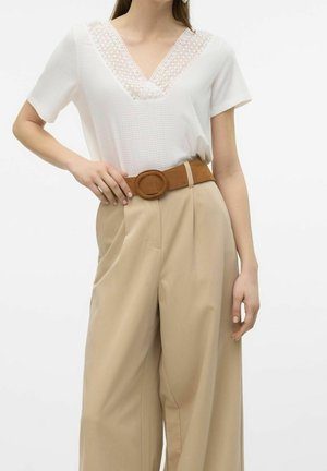 Frau trägt ein weißes Kurzarmtop mit Spitzen-V-Ausschnitt und hoch taillierte beige Hose mit weitem Bein und braunem Gürtel.