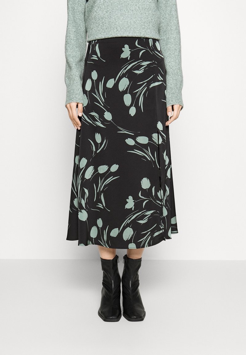 Černá midi sukně s květinovým vzorem v jemné zelené barvě, vyrobená z hladké látky. Má volný střih a rozšířený tvar, nosí se s černými botami.