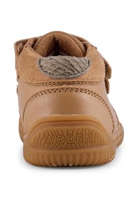 Scarpa da bambino in pelle marrone con un accentuato tallone testurizzato e strap in velcro, dotata di una suola in gomma con un motivo battistrada. Marchio "WODEN" visibile.