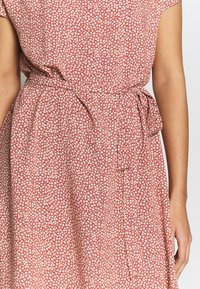 Vestido rojo con un estampado floral, mangas cortas y un lazo en la cintura. La tela parece ligera con un acabado texturizado.