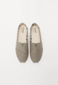 Baskets en toile grises à enfiler avec un motif subtil, présentant des accents verts, un dessus texturé et une semelle intérieure rembourrée étiquetée "TOMS."
