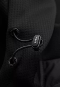 Tessuto nero con una superficie testurizzata e un sistema di chiusura a coulisse. Corda regolabile passa attraverso un occhiello per la sicurezza. Design minimalista.