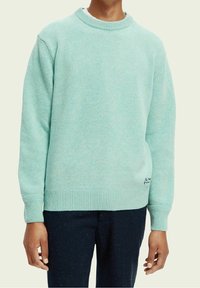 Maglione a maglia di colore azzurro chiaro con scollo a girocollo, polsini e fondo a costine. Presenta una superficie testurizzata e un piccolo dettaglio ricamato in basso.