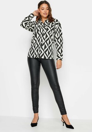 Camicia a maniche lunghe con bottoni in un motivo geometrico bianco e nero, abbinata a leggings in ecopelle neri e tacchi a punta neri.