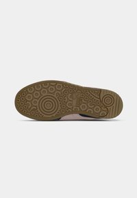 Sneaker sole in beige rubber with circular and wavy patterns; features a textured grip and embossed logo detail for traction.