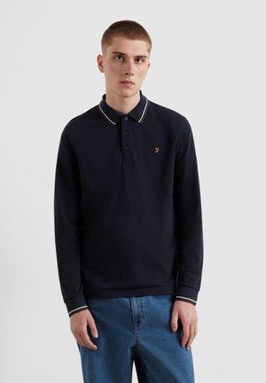 Marineblauwe poloshirt met lange mouwen, een kraag, drie knopen en contrasterende strepenaccenten op de kraag en manchetten. Klein geborduurd logo op de borst.