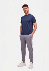 Maglietta in cotone blu navy a maniche corte, abbinata a pantaloni della tuta grigio chiaro con tasche laterali e sneakers bianche.