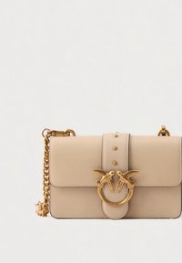 Bézs bőrből készült kézitáska téglalap alakú, arany madárdíszítéssel és láncos pánttal. Az elülső fülön szegecsekkel díszített részletek találhatók.