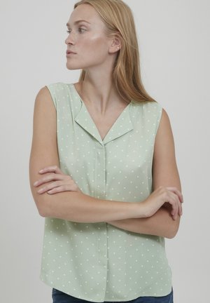 Blouse sans manches vert clair à pois blancs, avec un décolleté en V et une coupe décontractée. Fabriquée dans un tissu lisse et doux.