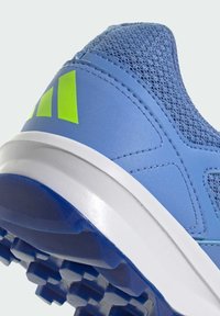Modrá športová obuv s textúrovaným sieťovinovým zvrškom, zelenými akcentmi, bielou medzipodrážkou a charakteristickou hrubou podrážkou pre trakciu.