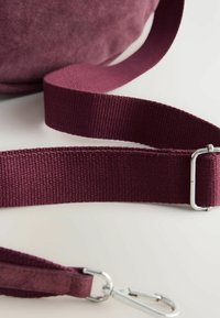 Bordeaux ruskinds taske med en matchende vævet strop. Stropen har en sølvklips og stikninger langs kanten.