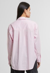 Lichtroze gestreepte oversized shirt met een achterplooien, knoopmanchetten en een klassieke kraag. Gemaakt van gladde stof met een relaxte pasvorm.