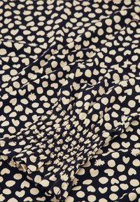 Marinefarbener Stoff mit cremefarbenem Druck, der verschiedene kleine Formen zeigt, darunter Herzen und andere Muster. Nahaufnahme von gerafftem Smocking-Detail.