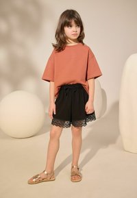Mørke sorte shorts med blondekant, parret med en rustfarvet oversized t-shirt og guld sandaler. Enkel, afslappet outfit.