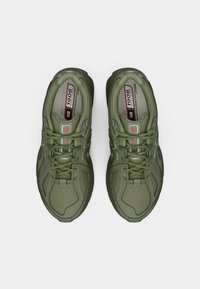 Une paire de baskets New Balance 1906 vertes avec des lacets, vues de dessus sur un fond blanc uni.