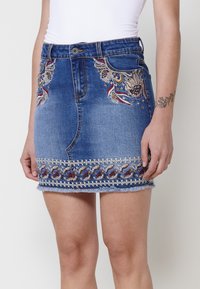 Jupe en denim mini avec broderies décoratives en rouge et or sur les côtés et l'ourlet, présentant un bas effiloché et un design standard à cinq poches.