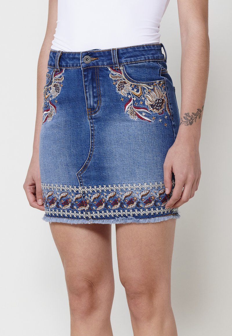 Jupe en denim mini avec broderies décoratives en rouge et or sur les côtés et l'ourlet, présentant un bas effiloché et un design standard à cinq poches.