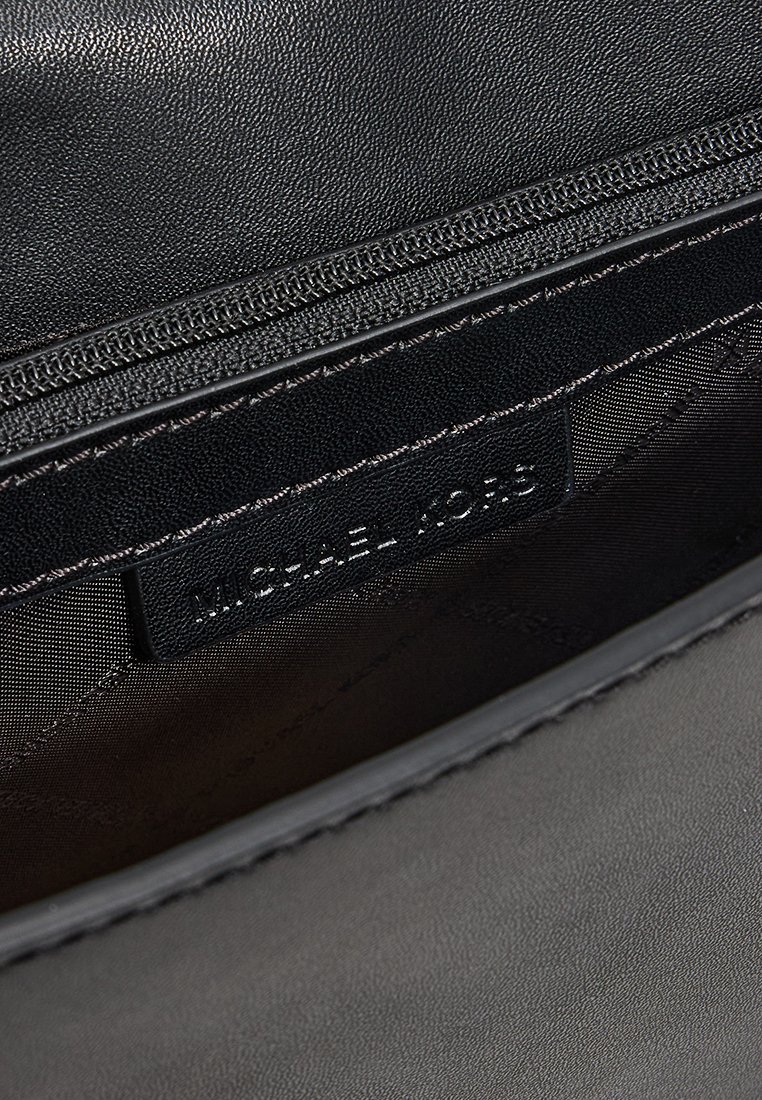 Intérieur d'un sac à main en cuir noir avec une poche zippée et une étiquette de marque visible avec du texte en relief. Texture lisse et design minimaliste.