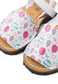White sandals featuring a colorful hot air balloon and heart pattern on the upper, with a brown leather insole and black rubber outsole.