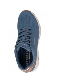 Zapatilla deportiva azul con diseño perforado, cordones texturizados y acento metálico en el talón. La entresuela blanca proporciona soporte acolchado.