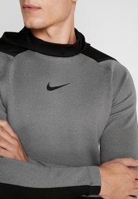 Camiseta atlética gris con un acento negro cerca del escote y los hombros. Presenta un pequeño logo negro de Nike en el pecho. Textura suave.
