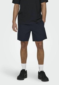 Shorts bleu marine en tissu doux, avec une coupe décontractée et des poches latérales. Associés à un t-shirt noir surdimensionné et des baskets sombres.