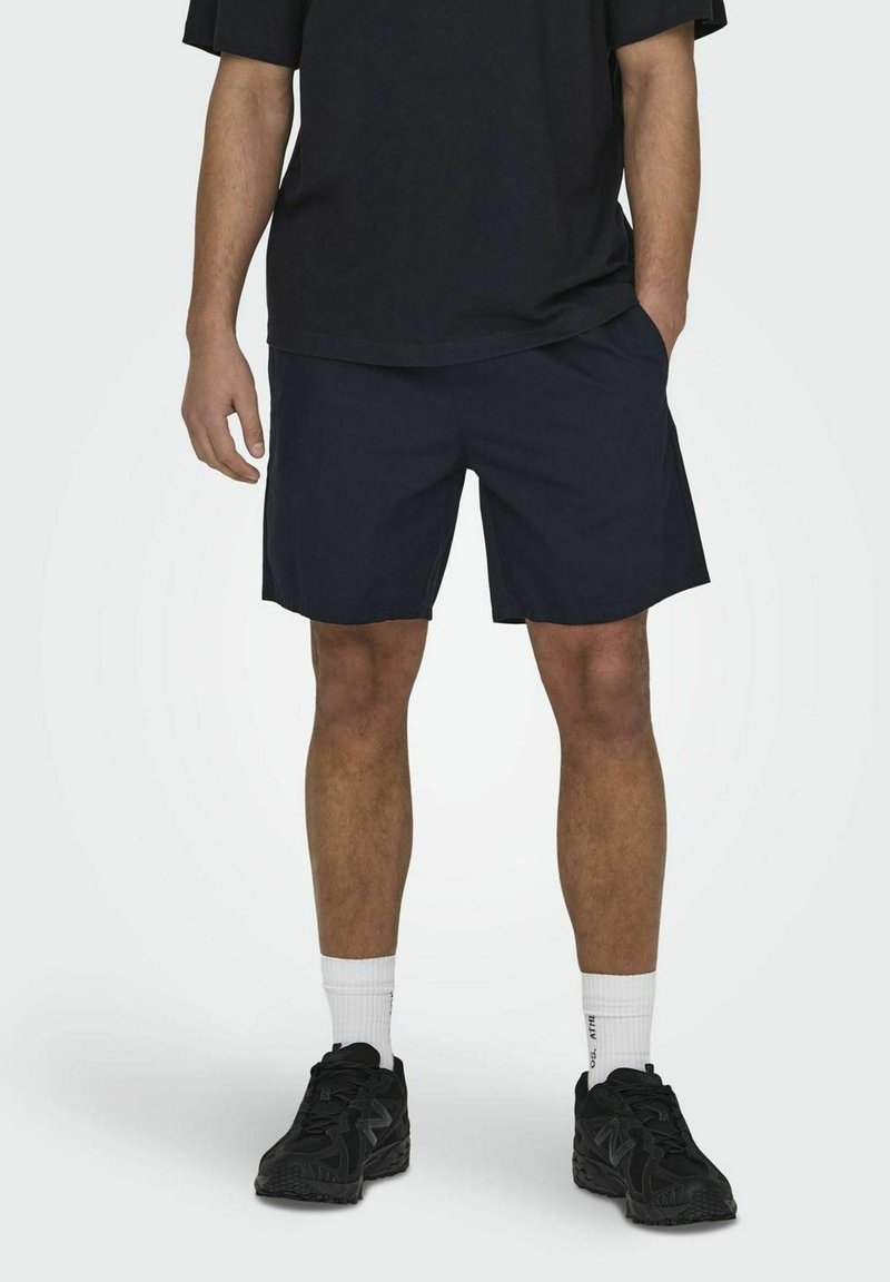 Shorts bleu marine en tissu doux, avec une coupe décontractée et des poches latérales. Associés à un t-shirt noir surdimensionné et des baskets sombres.