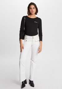 Maglietta nera a maniche lunghe con logo bianco, abbinata a pantaloni bianchi svasati con dettagli in bottone dorato e stivaletti neri con tacco.