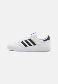 Vit sneakers med svart designtre ränder, texturerad läderöverdel, rundad tå, vadderad krage och sydda detaljer. Gyllene logotypaccent.