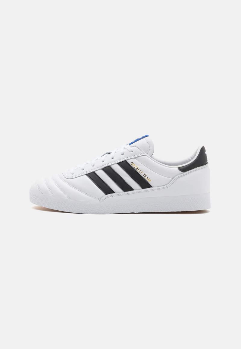 Vit sneakers med svart designtre ränder, texturerad läderöverdel, rundad tå, vadderad krage och sydda detaljer. Gyllene logotypaccent.