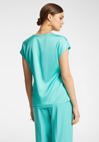 Top corto in satin turchese con maniche corte e vestibilità rilassata, caratterizzato da un collo rotondo e una texture liscia, abbinato a pantaloni larghi coordinati.