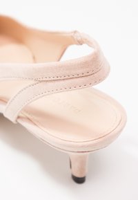 Sandale en daim beige avec une lanière étroite sur les orteils et un petit talon kitten avec une pointe noire.