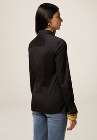 Black long-sleeve shirt with a collared neckline, featuring buttoned cuffs. Smooth fabric with a tailored fit, paired with light blue jeans.