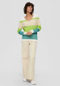 Sweter robiony na drutach z dekoltem w serek, ozdobiony poziomymi paskami w kolorach zielonym, niebieskim i kremowym. W komplecie z kremowymi spodniami z szerokimi nogawkami oraz białymi trampkami.