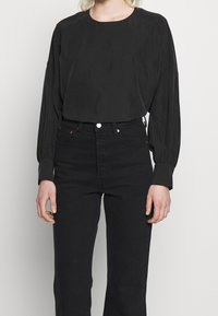 Svart långärmad topp med rund halsringning, tillverkad av slätt tyg, i kombination med högmidjade svarta jeans med en figurnära silhuett.