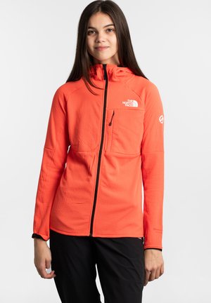 Veste zippée orange vif avec un motif texturé, capuche et détail de logo sur la poitrine. Dispose d'une poche frontale et de poignets élastiques.