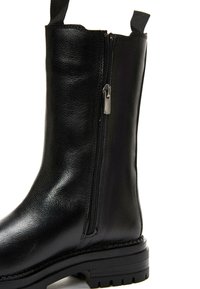 Black leather ankle boot with a zip closure, textured finish, and a sturdy black rubber sole. Includes a pull tab for easy wear.