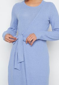 Robe côtelée bleu clair à manches longues, avec un design portefeuille et une taille nouée, fabriquée en tissu tricoté texturé.