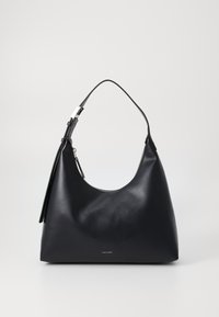 Borsa hobo in pelle nera con silhouette curva, chiusura zip e tracolla regolabile. Presenta un piccolo tag con il nome del brand 'Calvin Klein.'