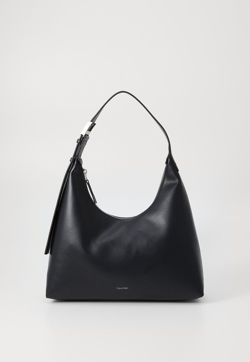 Borsa hobo in pelle nera con silhouette curva, chiusura zip e tracolla regolabile. Presenta un piccolo tag con il nome del brand 'Calvin Klein.'