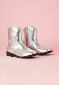 Zilveren cowboylaarzen met een glanzende, metallic afwerking. Voorzien van ster- borduursel, een zijrits en een lage zwarte hak. Glad textuur.