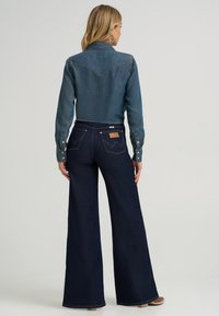 Denim shirt in medium blue with a pointed collar and snap buttons, paired with wide-leg dark blue jeans featuring back pocket accents.
